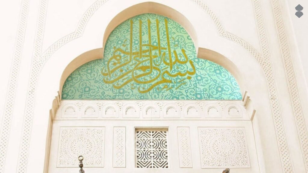 Elegant gold Arabic calligraphy set against a turquoise mosaic background inside an archway above a carved white door.