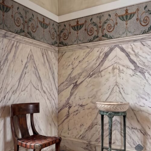 A classical mosaic border frieze of urns and acanthus scrolls running along a wall above marble paneling