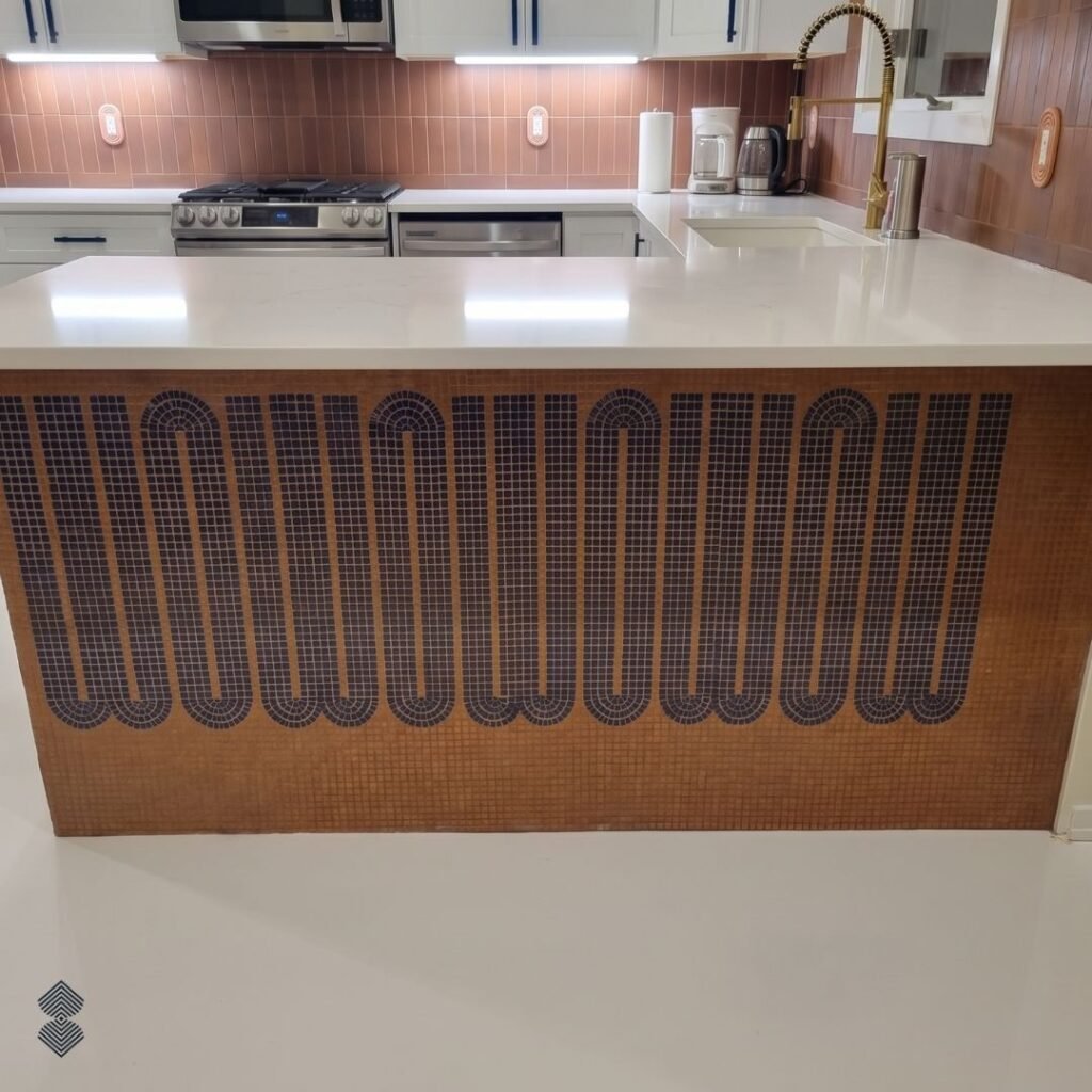 A kitchen countertop showcasing a custom mosaic front with a continuous, wavy geometric line pattern in dark blue against a warm copper-toned background.