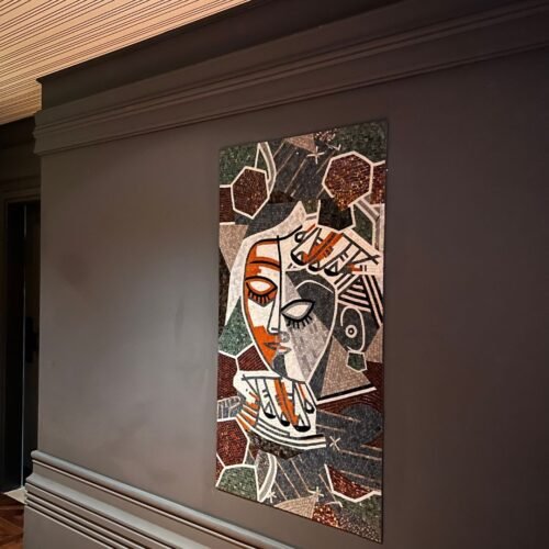 A cubist face mosaic mural in charcoal, rust and cream tones mounted on a dark cafe wall.