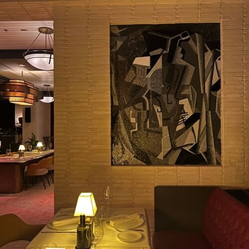 A cubist mosaic wall art panel of fragmented gray and gold glass tesserae set in a recessed niche.