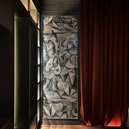 A floor-to-ceiling cubist musicians mosaic mural in gray and black stone tesserae set into a dark wall alcove.