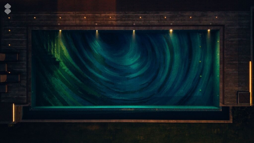Nighttime aerial view of a illuminated rectangular pool showing a dark blue swirl mosaic.