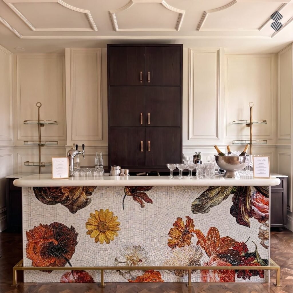 A bar counter featuring a large-scale, intricate floral mosaic front with vibrant orange, yellow, and deep red flowers on a white background, complete with a sleek brass footrail.