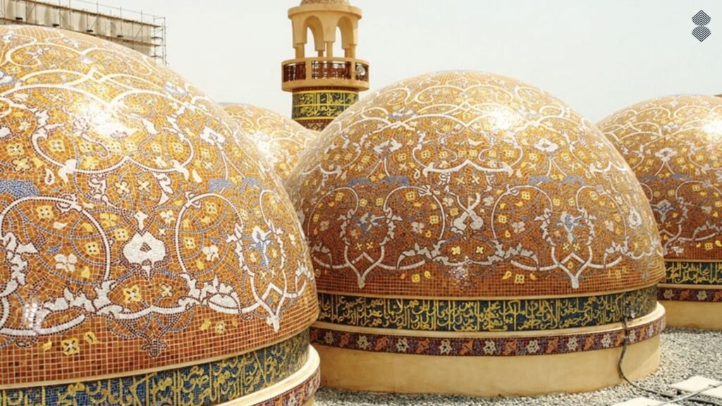 Close-up of large mosque domes covered in elaborate, warm golden-orange mosaic floral patterns with Arabic script encircling the base.