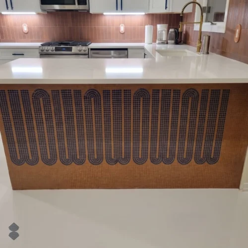 Handcrafted geometric mosaic kitchen island with dark looping arches set against a warm terracotta tesserae background.