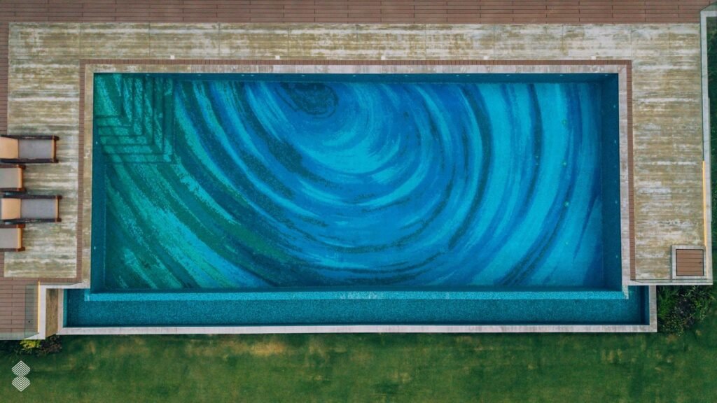 Overhead view of a rectangular backyard pool with a full-floor blue and teal mosaic pattern.