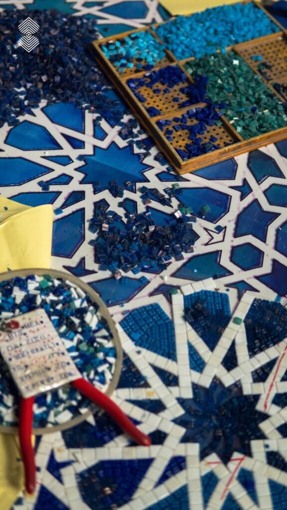 Overhead view of small blue and teal mosaic tiles being assembled into an Islamic geometric star pattern on a white surface.