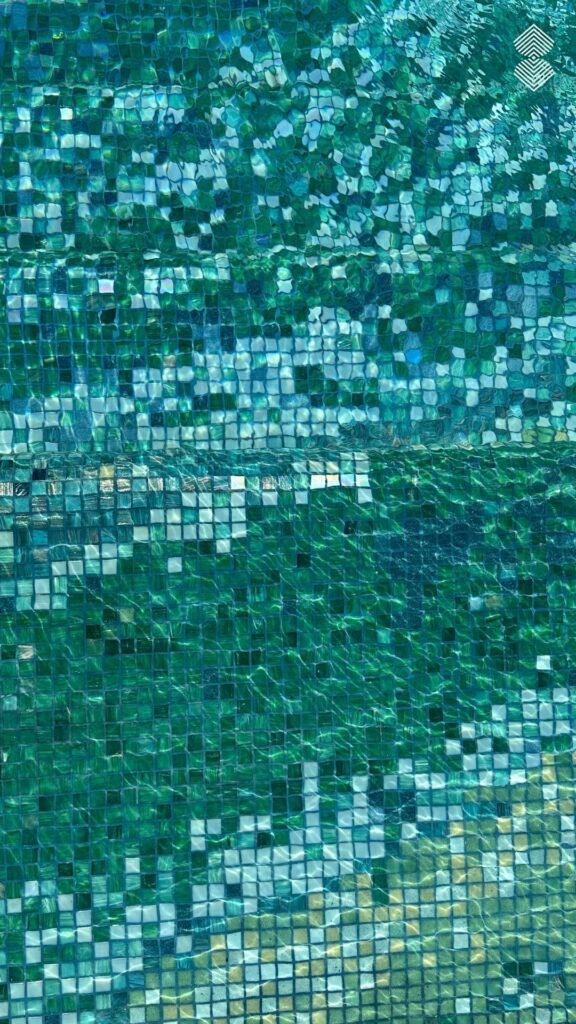 Top-down macro view of turquoise and green square glass tiles refracting through moving water.