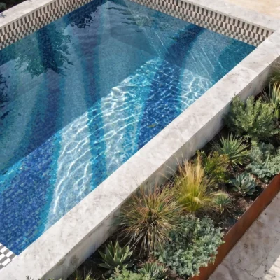 The Parallax glass mosaic pool with flowing aqua, turquoise, cobalt, and deep blue patterns in a luxury landscaped outdoor setting.