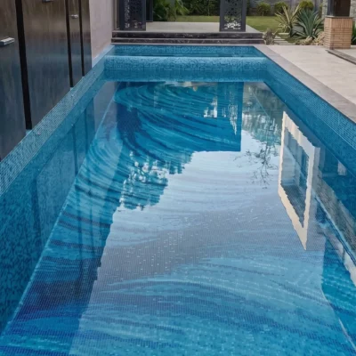 Prussian Wave glass mosaic pool featuring flowing blue, turquoise, and aqua bands across the floor of a contemporary outdoor swimming pool.