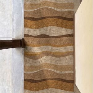 A narrow wave pattern walkway mosaic in caramel, gold and cream marble tesserae set underfoot in a corridor.