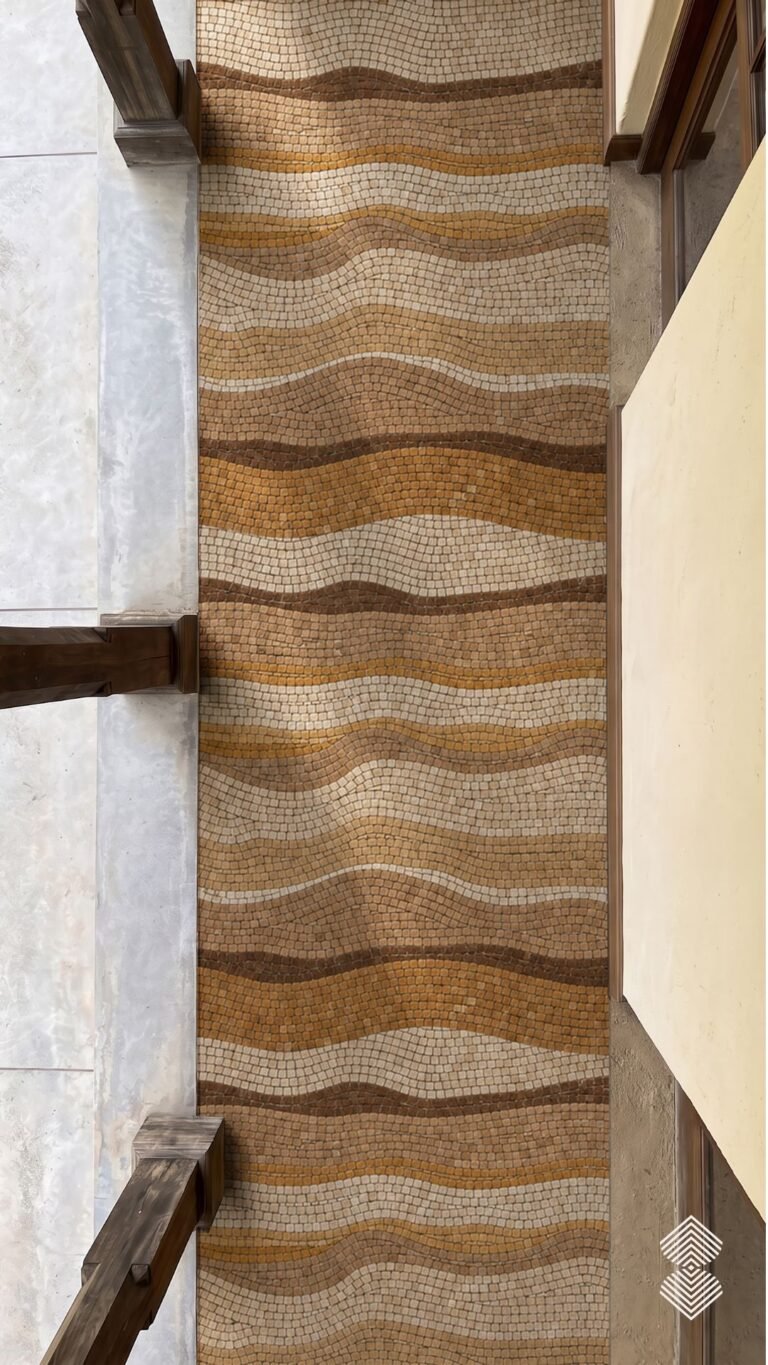 A narrow wave pattern walkway mosaic in caramel, gold and cream marble tesserae set underfoot in a corridor.