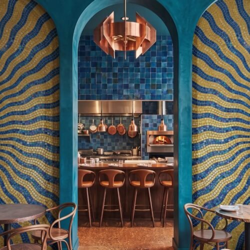 A wavy stripe wall mosaic in cobalt blue and ochre gold fills a curved archway recess.