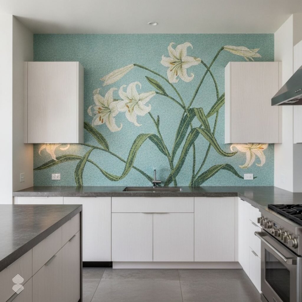 A modern kitchen featuring a custom mosaic backsplash with large white lilies and green stems set against a textured light blue background, positioned between sleek white cabinetry.