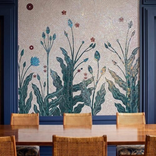 A botanical wall mural mosaic of tall green stems, leaves and small red flowers on a cream tiled wall.