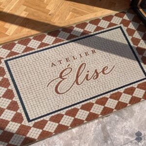 A script logo entryway mosaic in tumbled cream and terracotta stone, framed by a charcoal border and a diamond lattice.