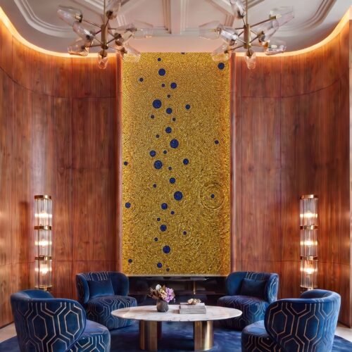 A tall gold mosaic feature wall with concentric circles and deep blue dot accents mounted in a wood-paneled lounge niche