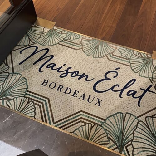 Maison Éclat Signature Mosaic Panel with ginkgo leaf border set into a shop entrance floor between wood and marble
