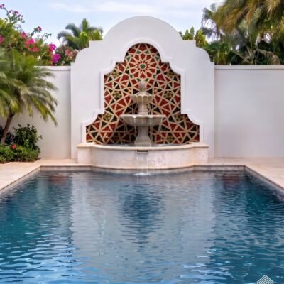 Arched mosaic star fountain backsplash in red, cream and gold tile above a stone pool fountain basin
